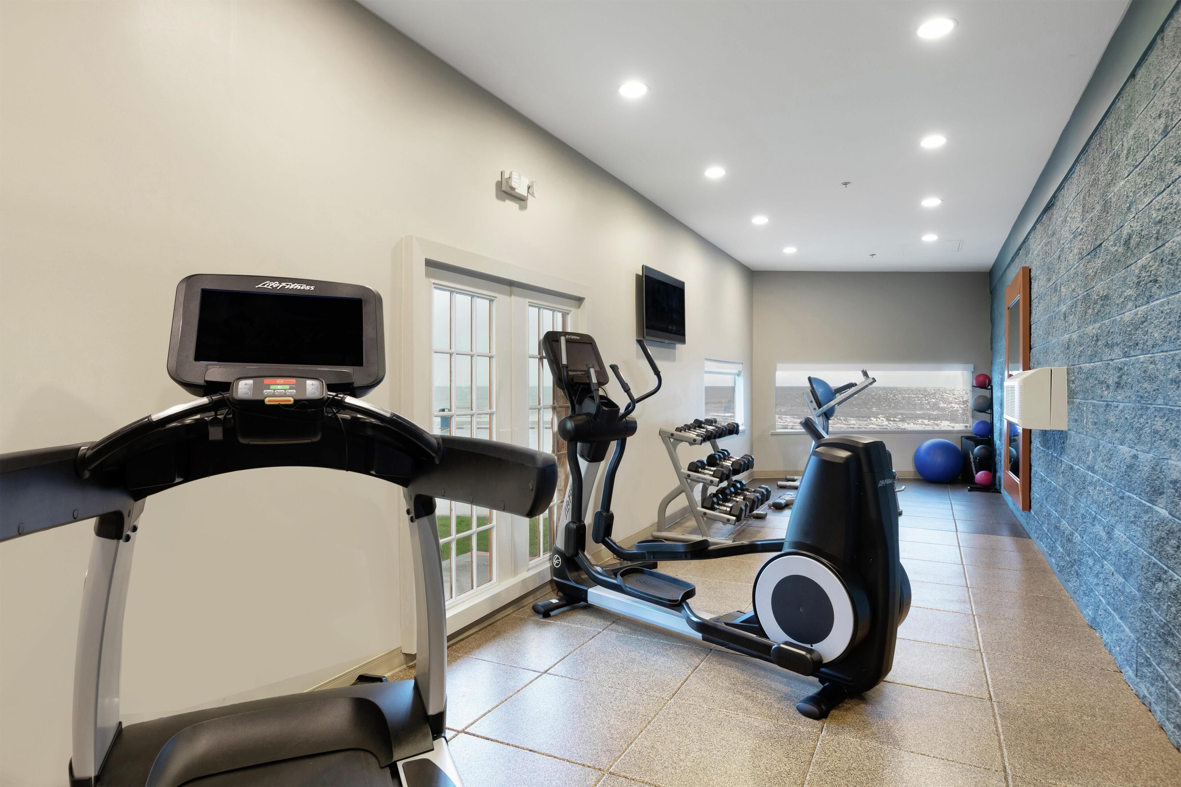 Un gimnasio con equipamiento de ejercicio, televisión y ventana con vistas.