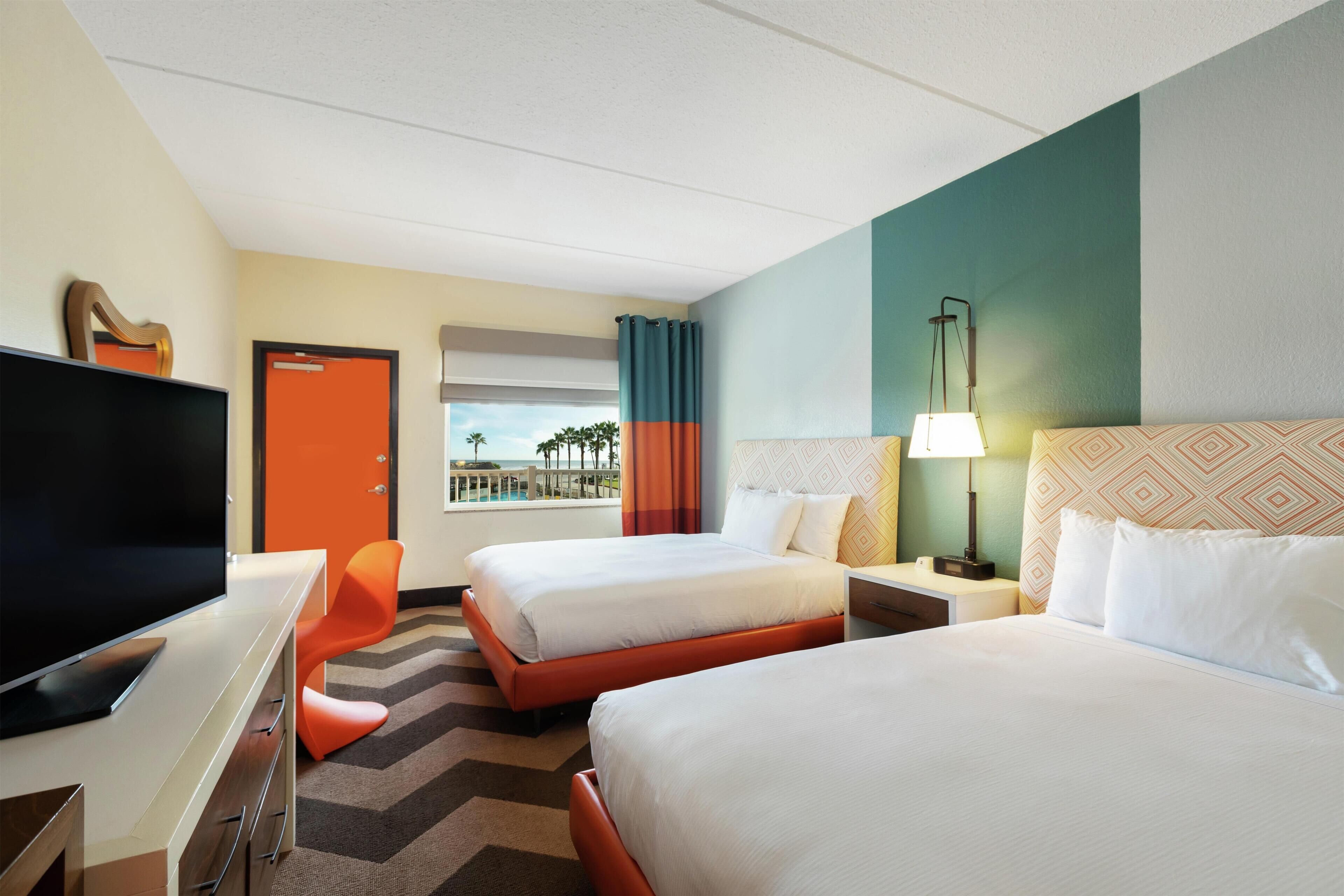 A hotel room with two beds, a desk with a TV, a nightstand, and a view of the ocean.