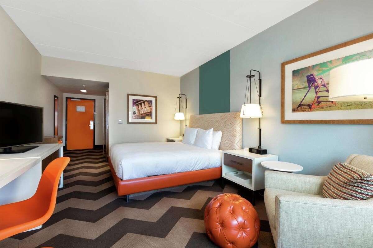 Een hotelkamer met een bed, een bureau met een televisie, een stoel, een bank, een lamp en een schilderij aan de muur.