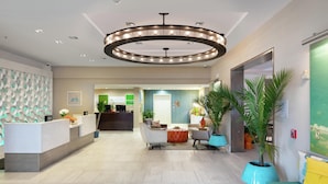 A modern hotel lobby with a reception desk, seating area, and a large circular chandelier.