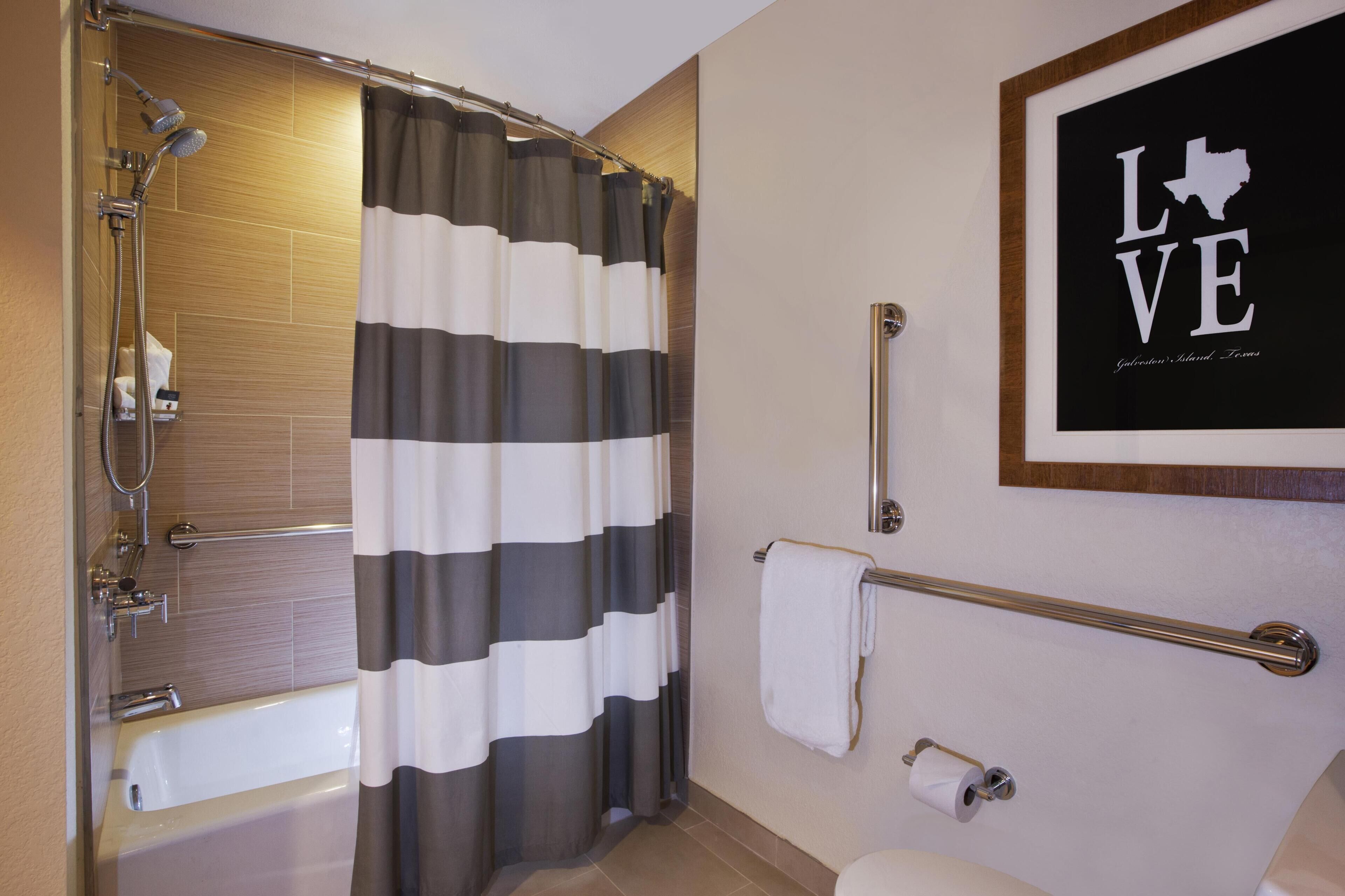A bathroom with a shower, a bathtub, a toilet, a towel rack, and a framed sign on the wall.