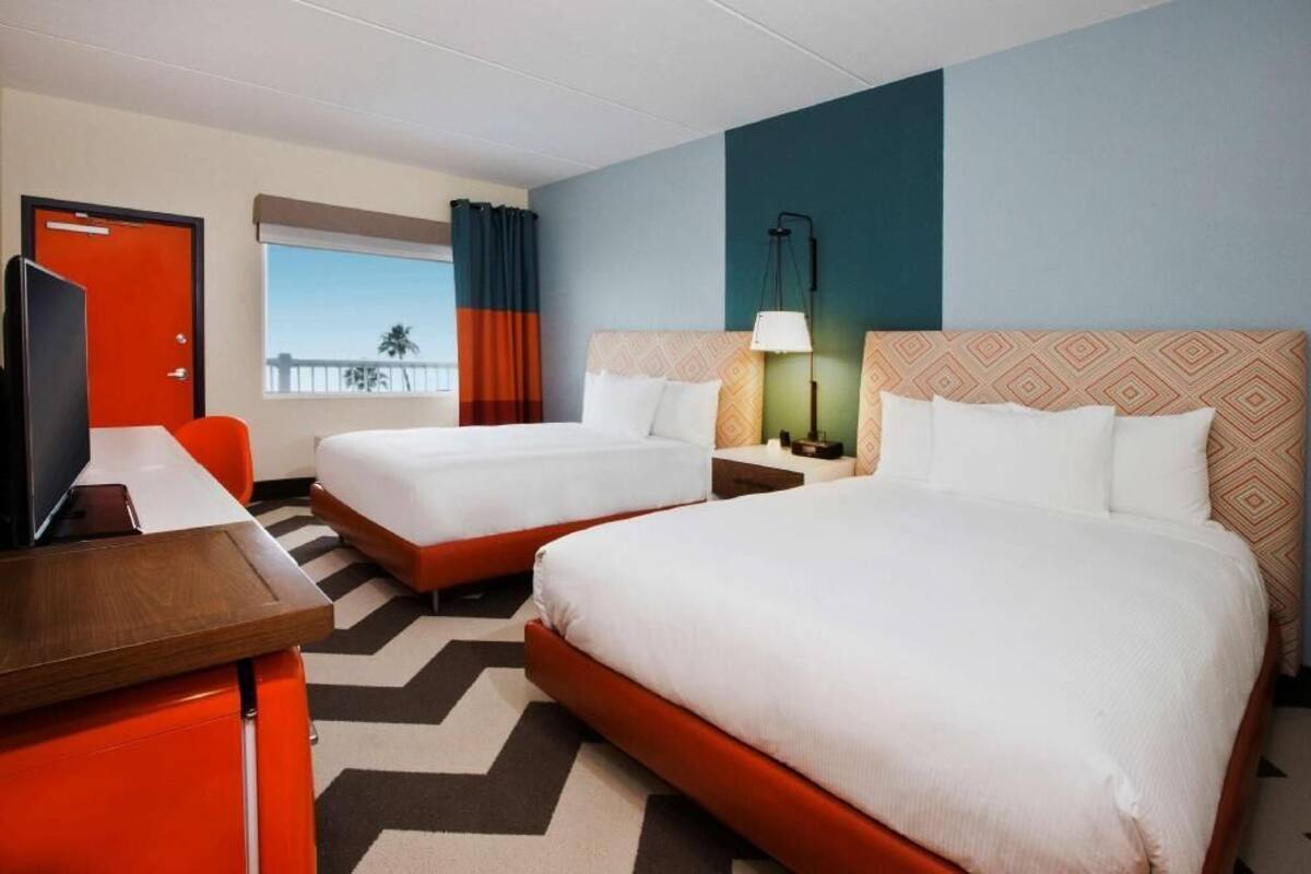Een hotelkamer met twee bedden, een bureau, een televisie, een raam met uitzicht en een gestreept hoofdeinde.