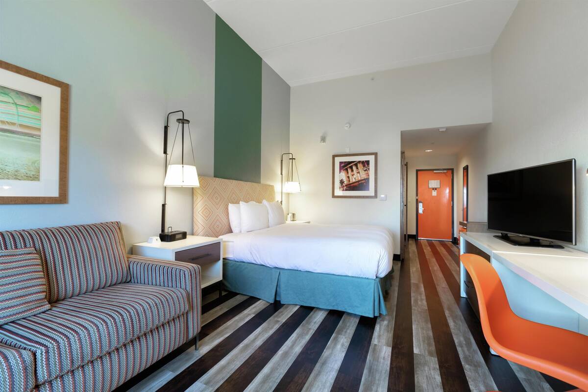 Een hotelkamer met een bed, een slaapbank, een bureau, een televisie en een schilderij aan de muur.
