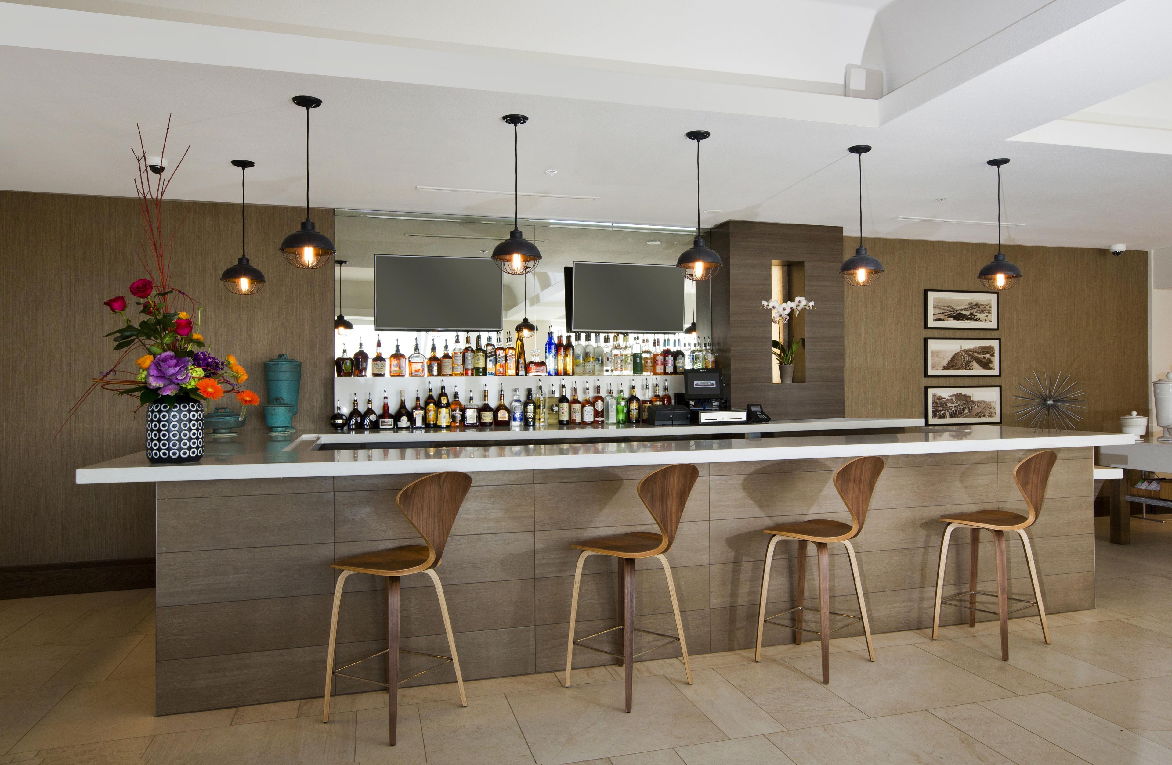 Een moderne bar met een lange toonbank, meerdere hangende lampen en drie houten barkrukken.