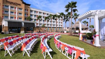 Une cour d’hôtel avec des rangées de chaises blanches, des palmiers et un bâtiment doté de balcons.