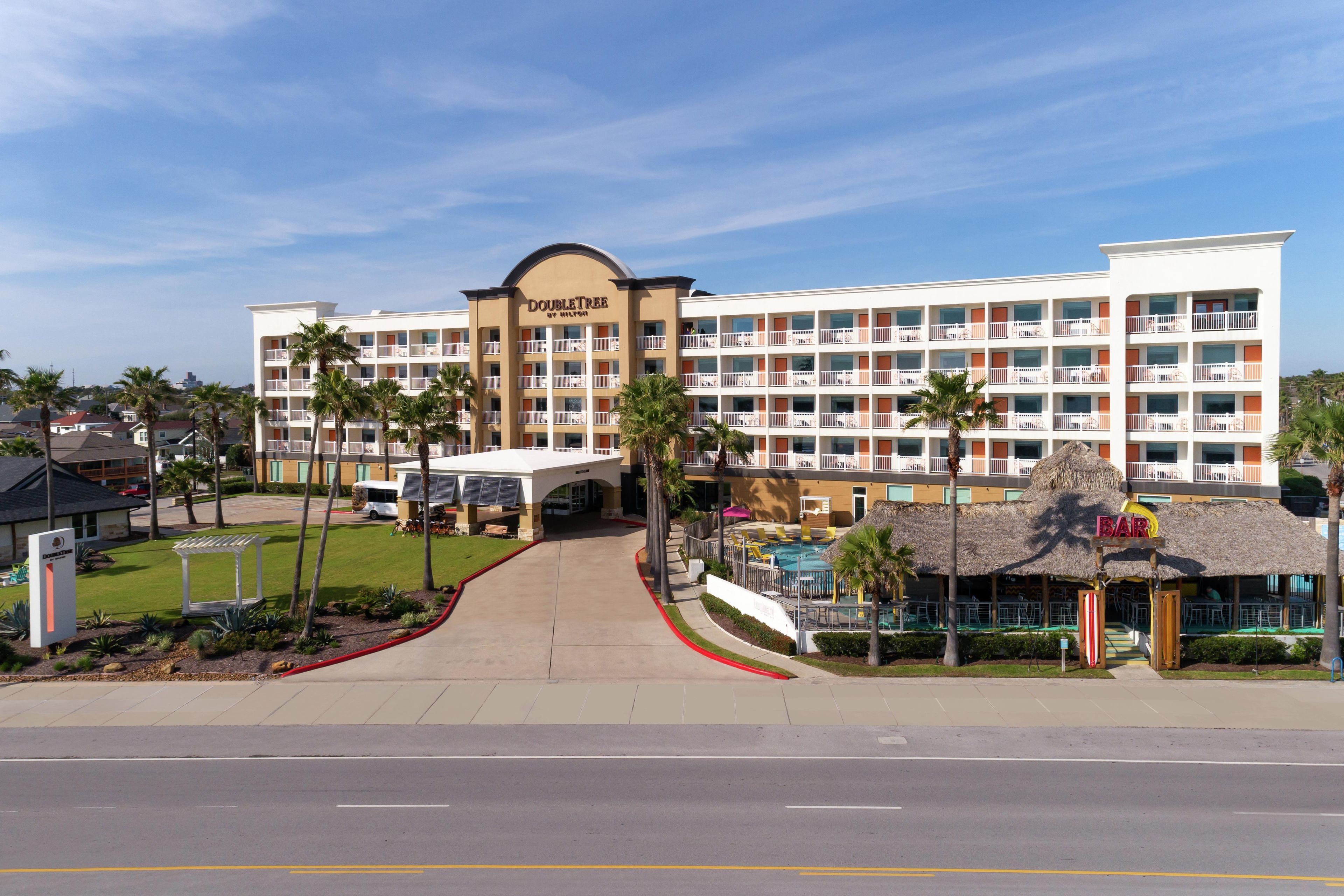 A hotel with a central entrance, multiple balconies, and a pool area.