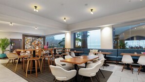 A modern restaurant with wooden tables and chairs, large windows with a view, and a decorative wall art piece.