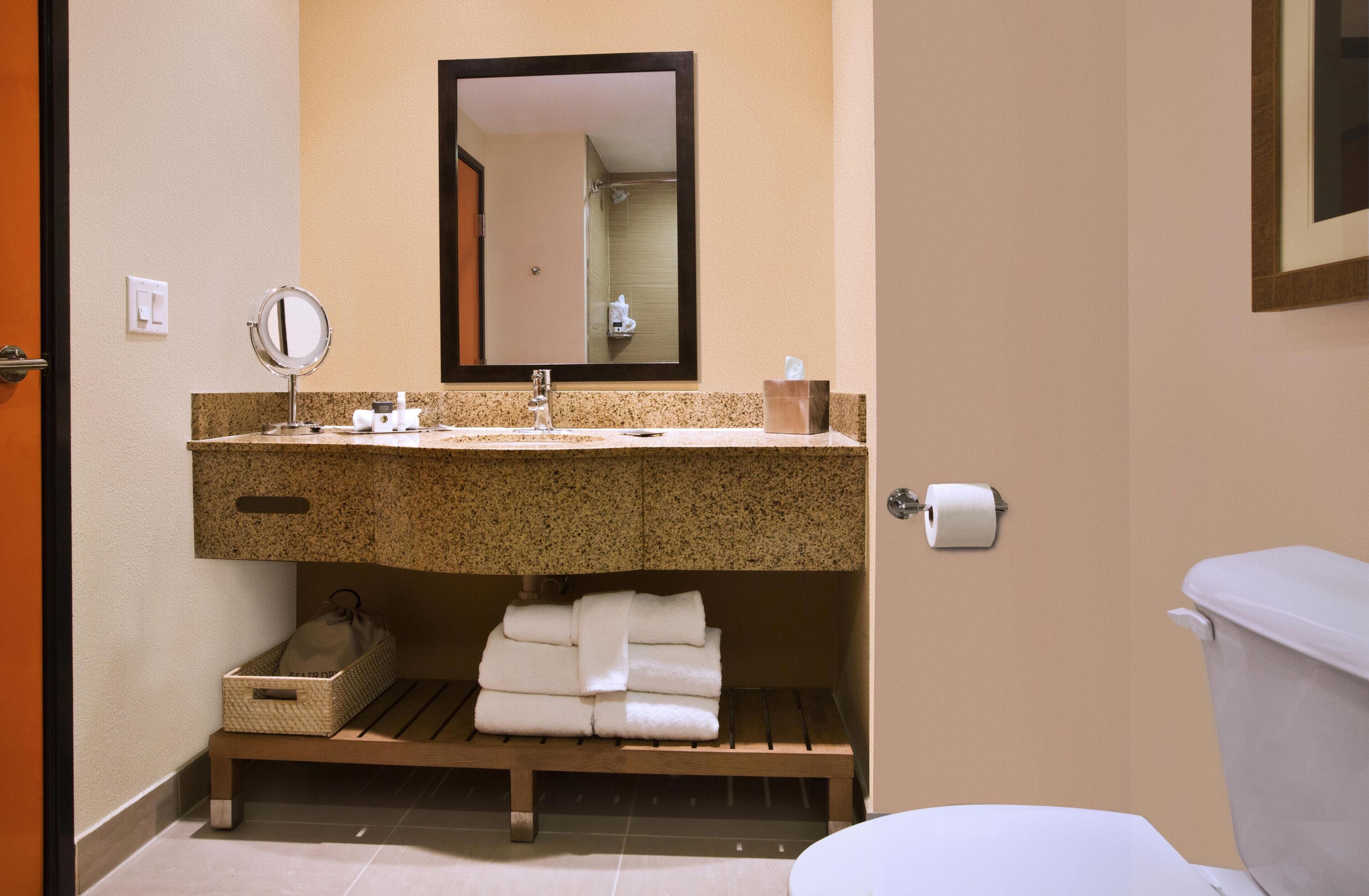 A bathroom with a sink, mirror, towel rack, toilet, and a small trash bin.