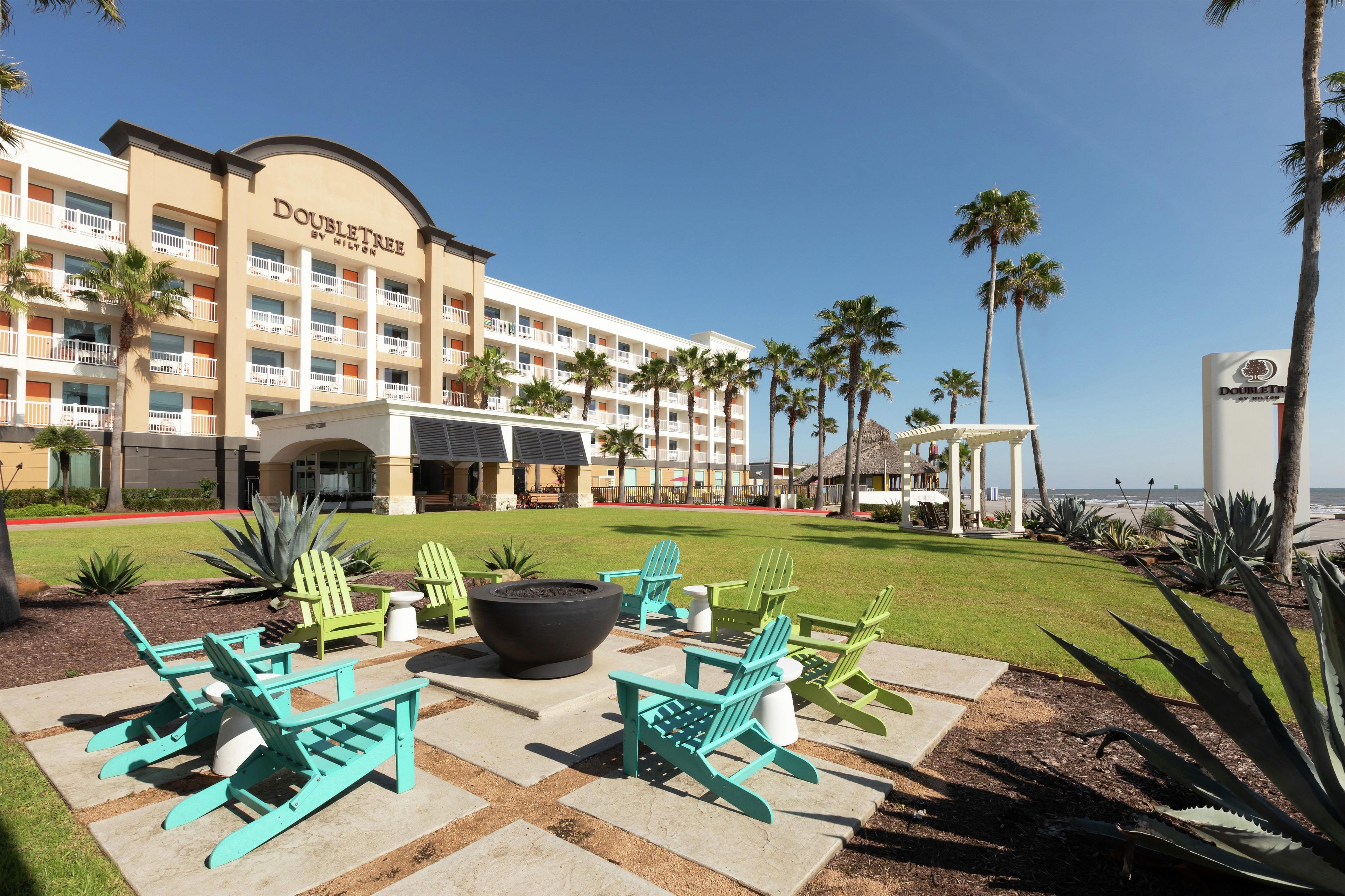 Een hotel met een zwembad, terras en palmbomen.