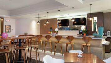 Ein modernes Restaurant mit Holztischen und -stühlen, einer Bar, einem Fernseher und einer sichtbaren Küche im Hintergrund.