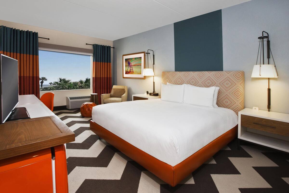 Een hotelkamer met een groot bed, een bureau, een stoel, een televisie en een raam met gordijnen.