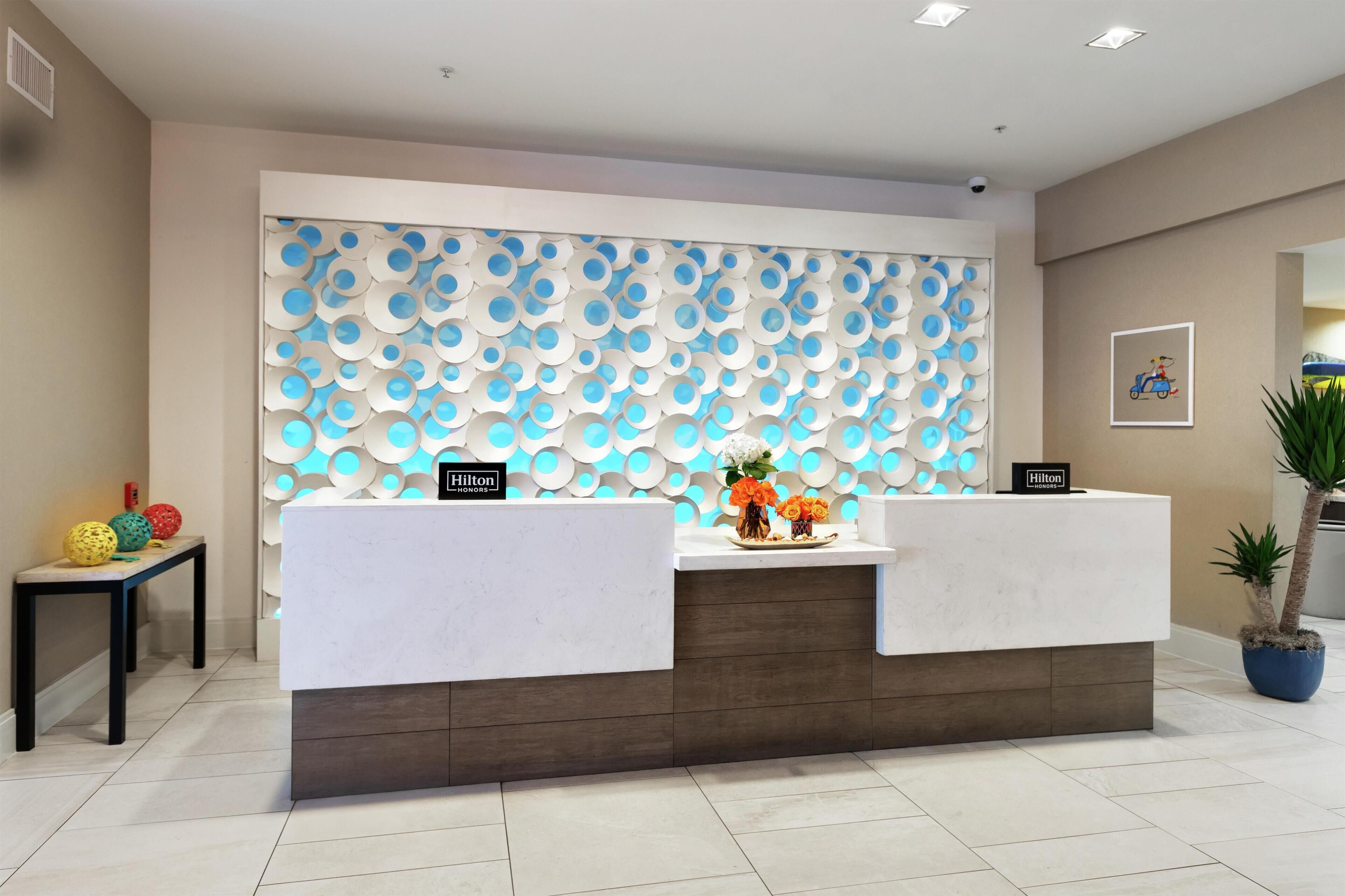 A hotel reception desk with a modern design, a potted plant, and a framed picture on the wall.