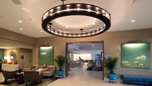 A hotel lobby with a circular ceiling light, seating area, reception desk, and a view into the dining area.