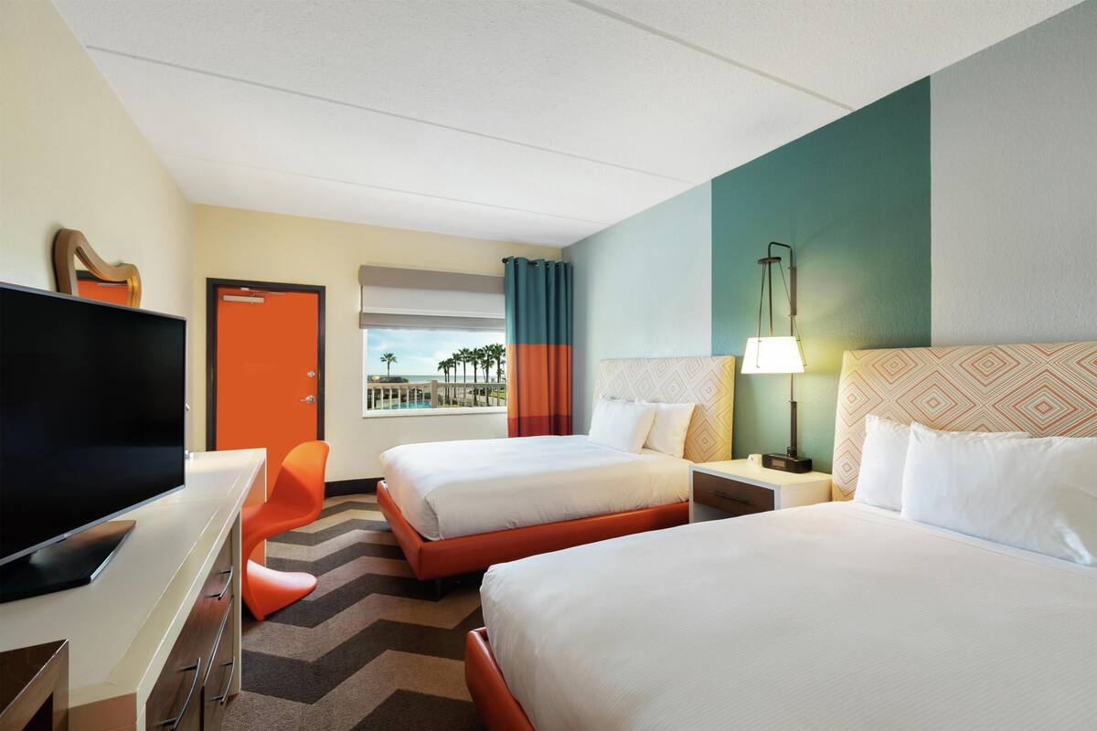 Een hotelkamer met twee bedden, een bureau met een flatscreen televisie, een stoel, een nachtkastje met een lamp en uitzicht op zee.