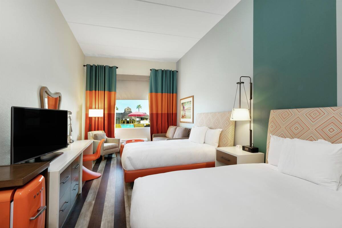 Hotelkamer met twee bedden, een televisie, een bureau met lades en uitzicht op een zwembad.