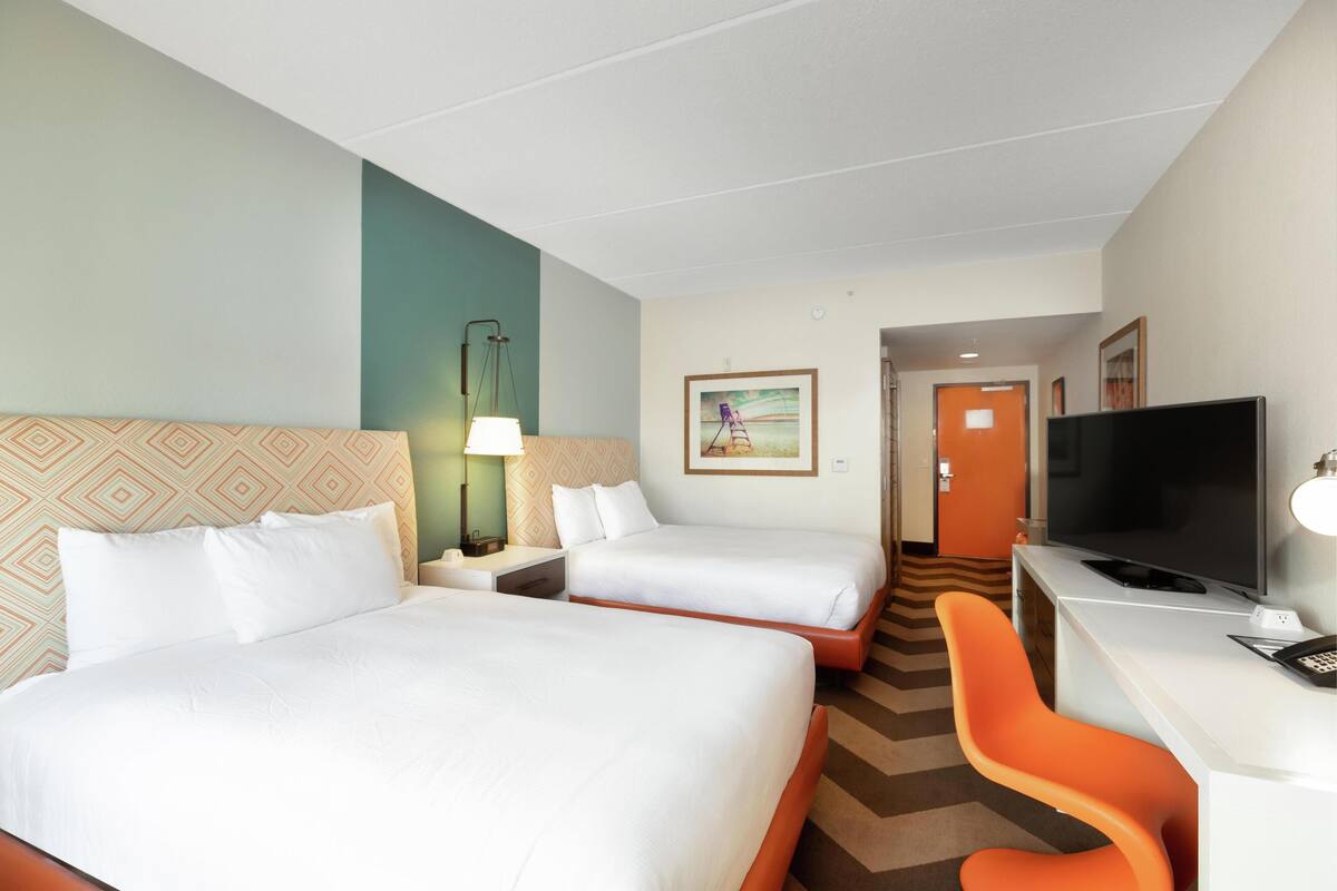 Een hotelkamer met twee bedden, een bureau met een televisie en een stoel.
