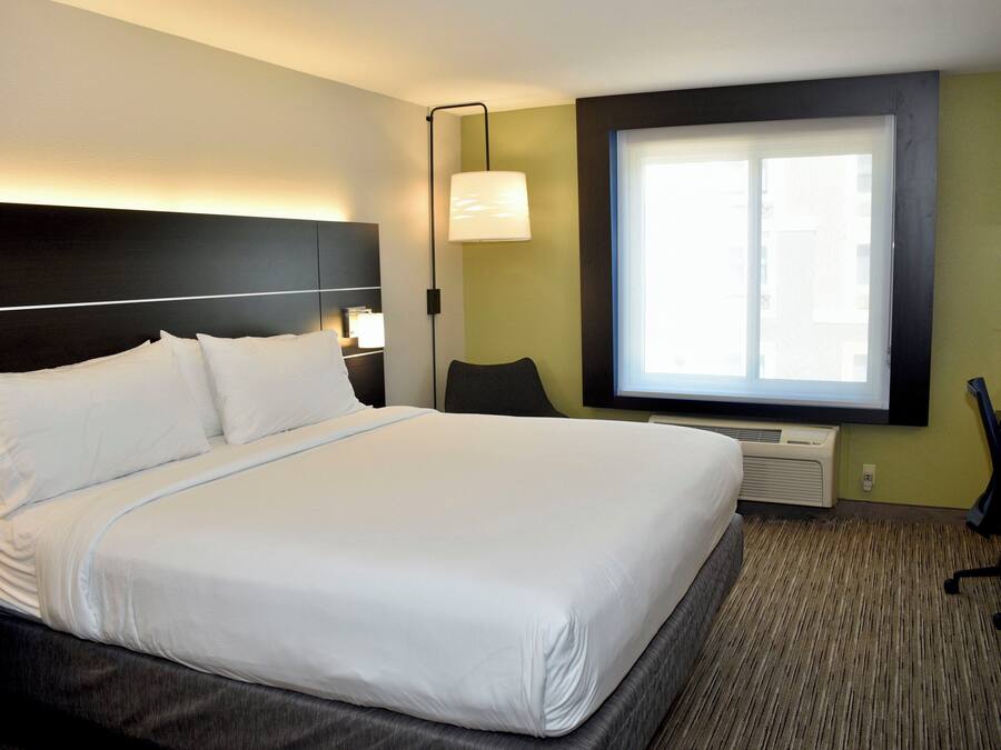Ein Hotelzimmer mit einem großen Bett, einem Schreibtisch, einem Stuhl, einer Lampe und einem Fenster.