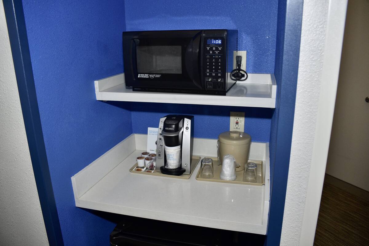A kitchen area with a microwave on a white shelf, a coffee maker, and a coffee pot on a lower shelf.