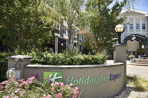 Señal de Holiday Inn Express con un área ajardinada al frente, que incluye una fuente y plantas con flores.