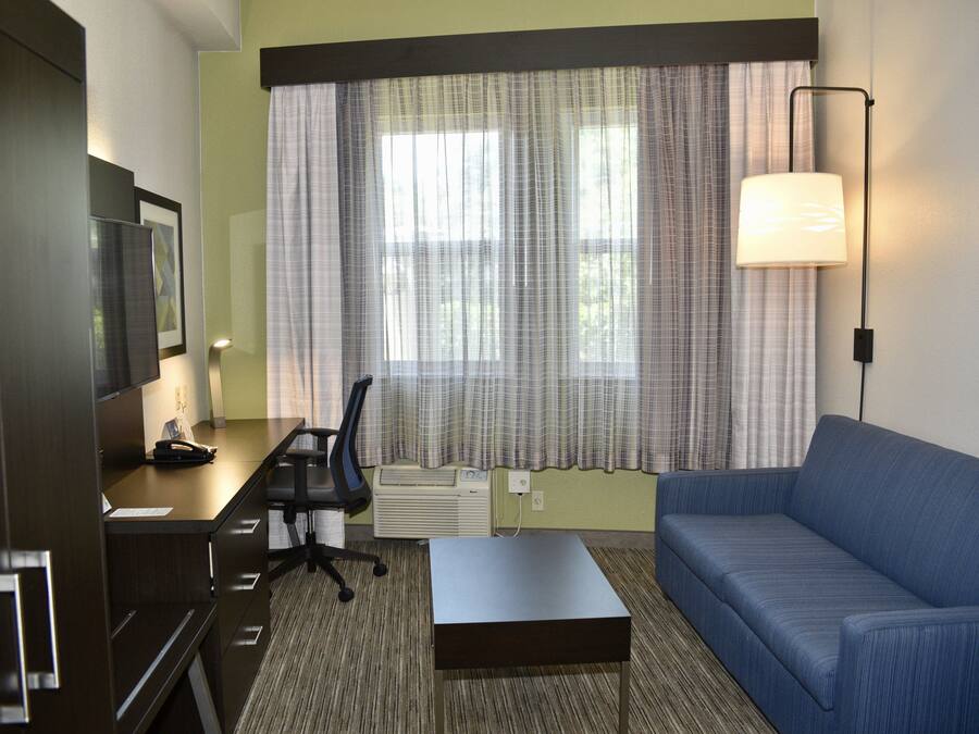 A hotel room with a desk, chair, sofa, and a standing lamp.