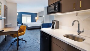 A compact hotel room with a kitchenette, a bed with a blue accent wall, a desk with a chair, and a small bathroom. - Holiday Inn Express & Suites Kent - University Area by IHG (Kent)