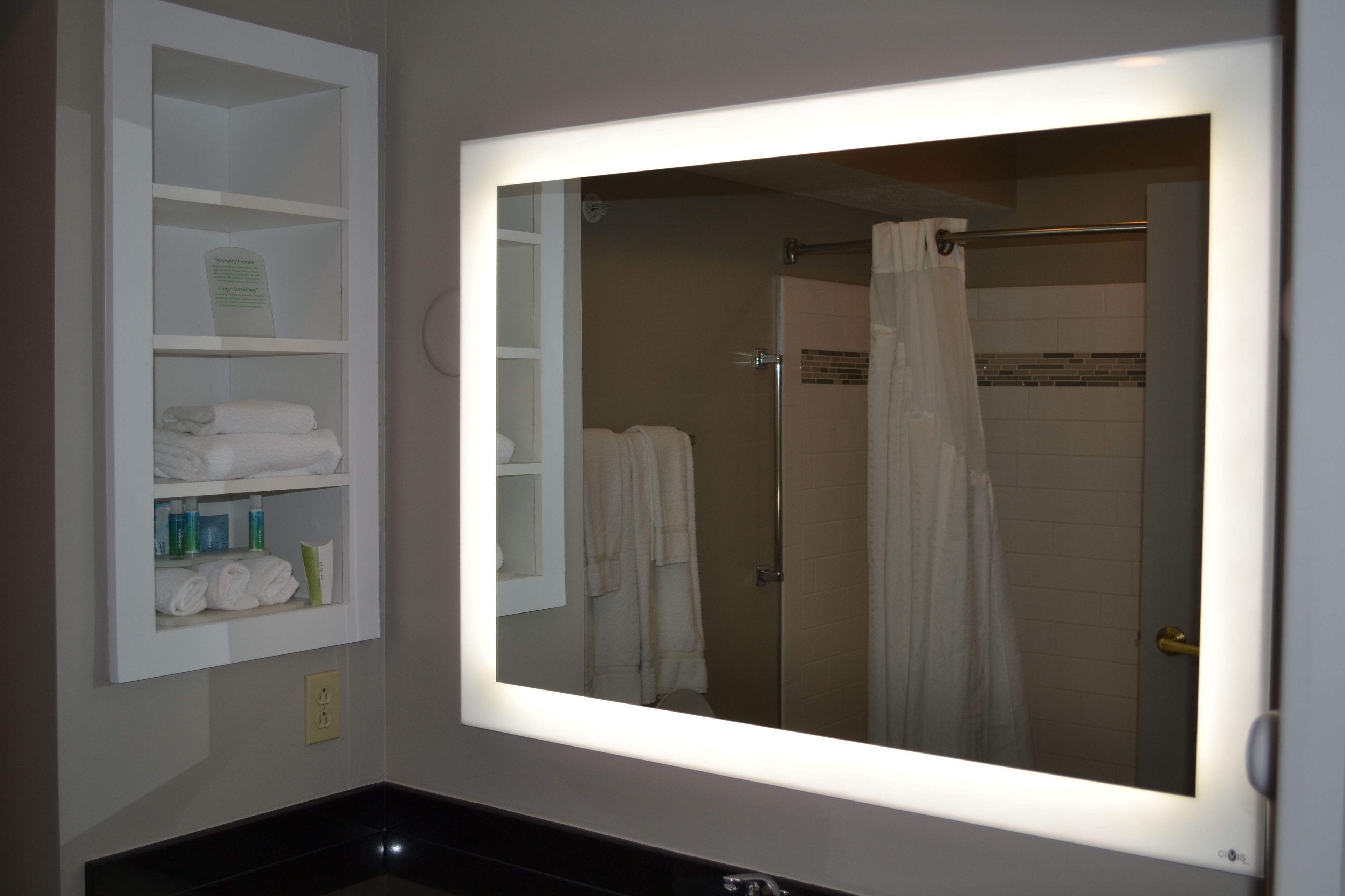 A bathroom with a large mirror, a shelf with towels, and a shower area.