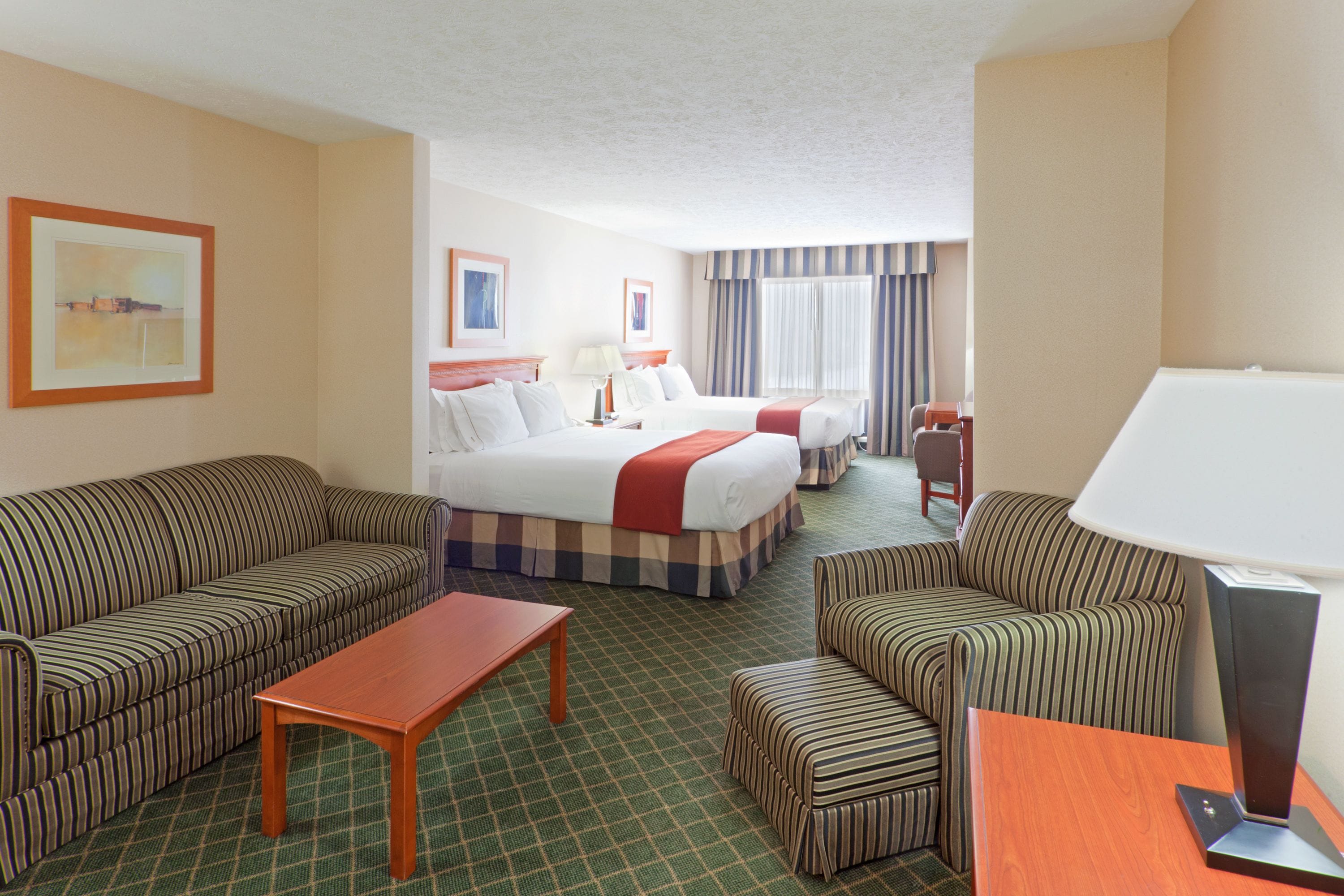A hotel room with a bed, two striped sofas, a small table, and a lamp.