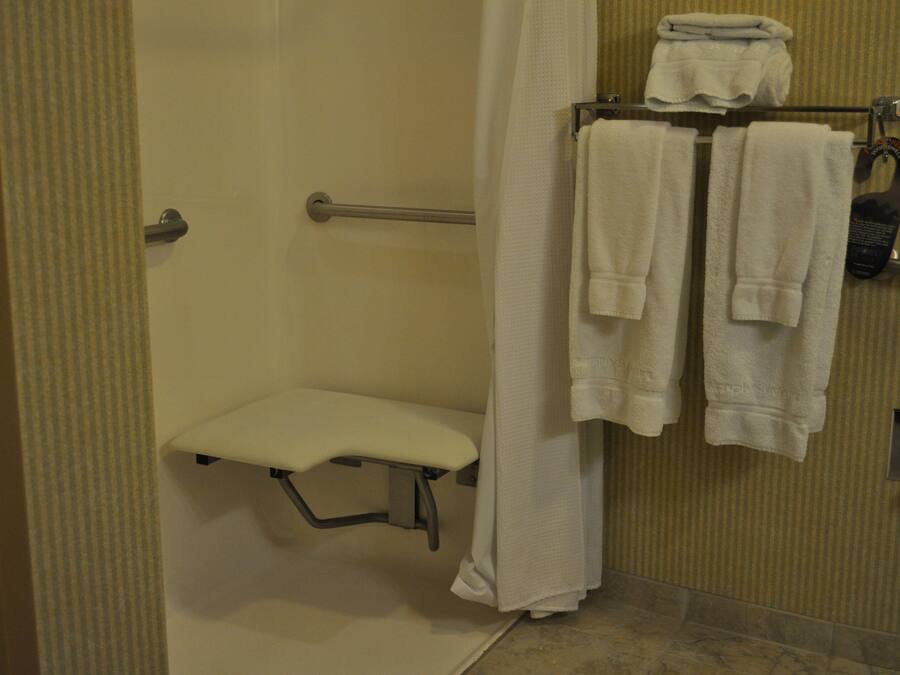 A shower area with a bench, a towel rack with towels, and a shower curtain.