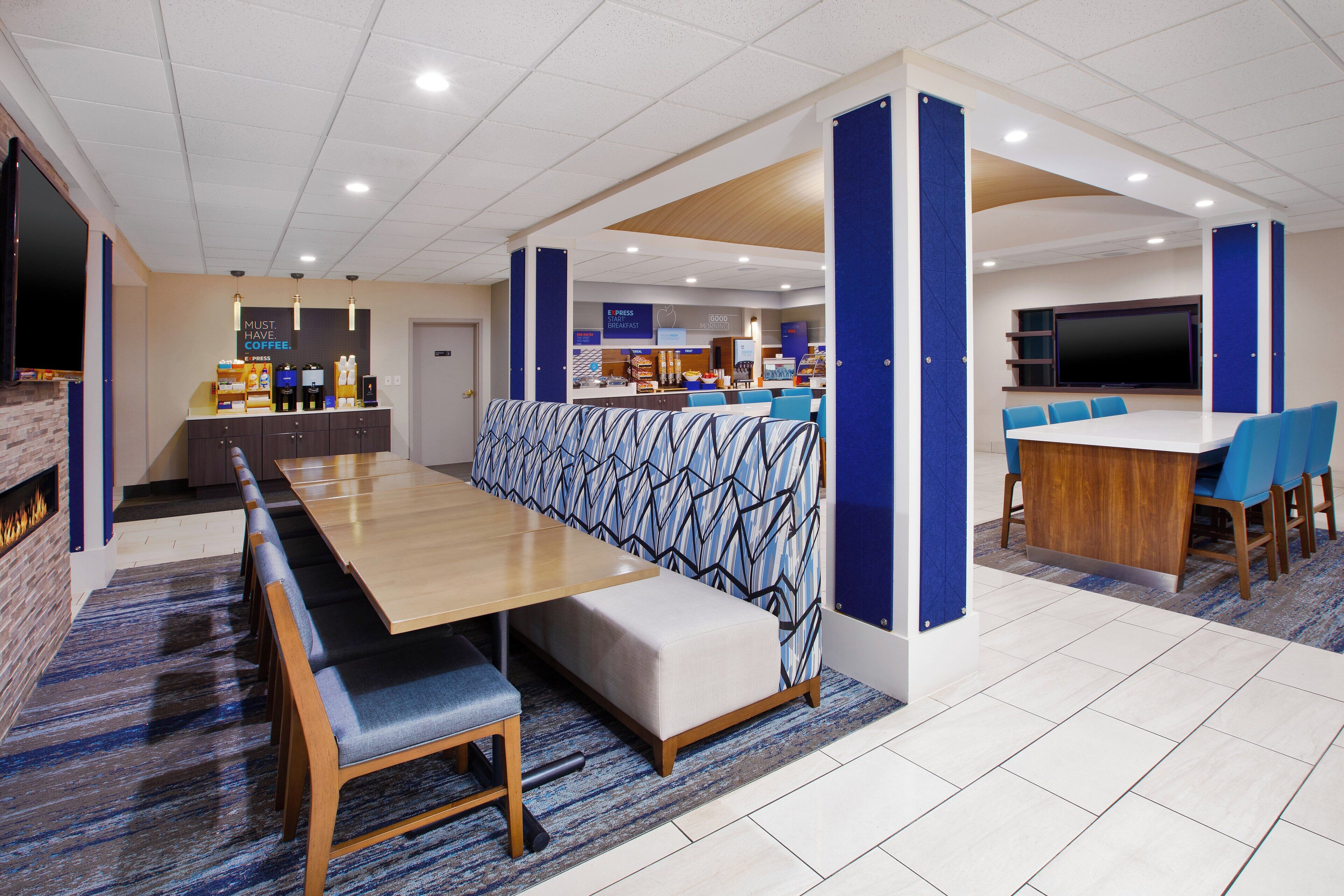 A modern hotel lobby with a long dining table, seating area, and a coffee bar.