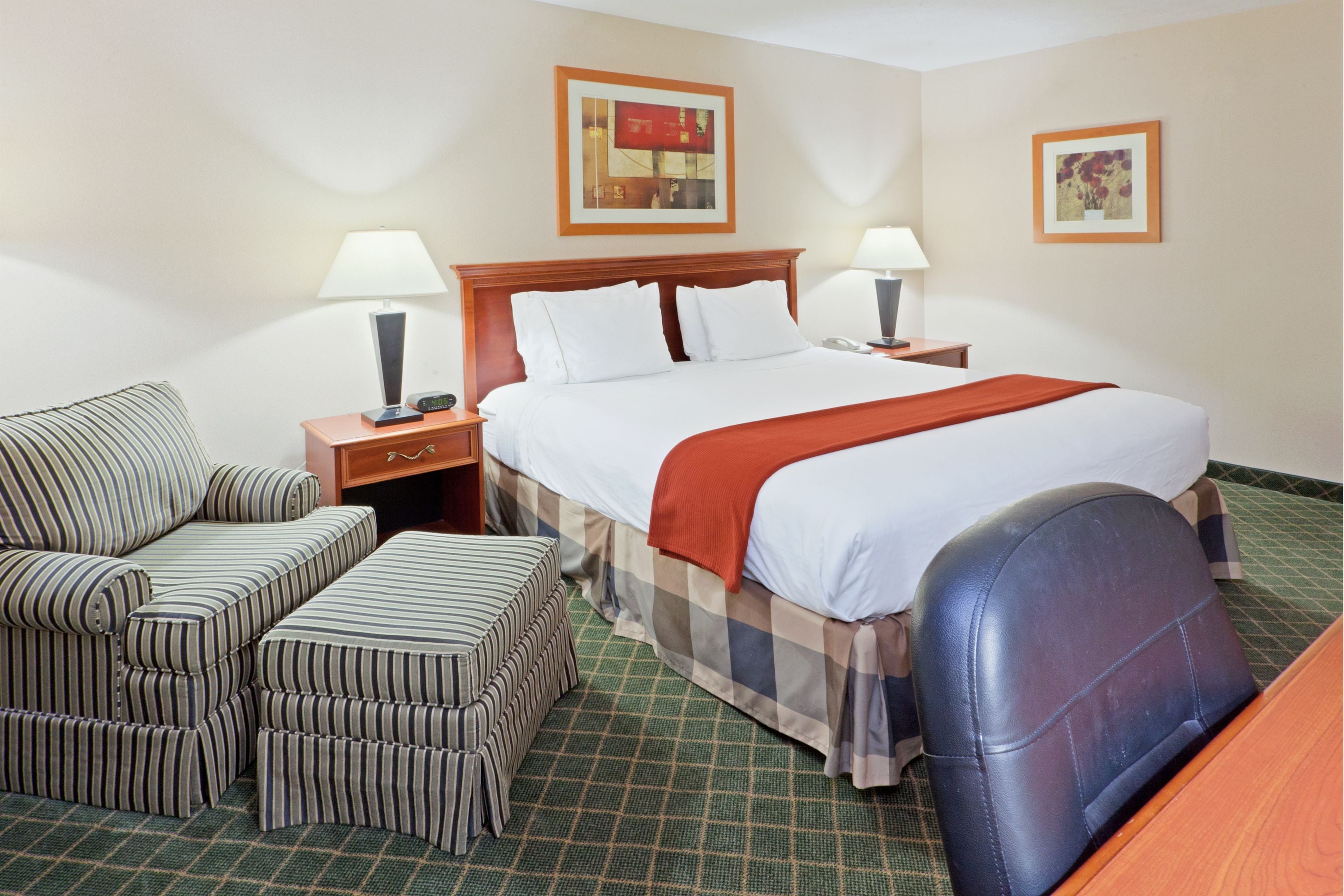 A hotel room with a bed, two bedside tables, a chair, and an ottoman.