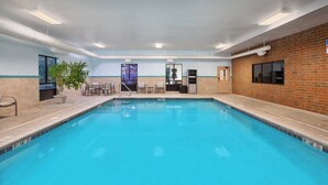 An indoor swimming pool with a tiled edge, a potted plant, and a seating area with chairs and a table. - Holiday Inn Express & Suites Kent - University Area by IHG (Kent)