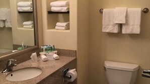 A bathroom with a sink, mirror, towel rack, toilet, and shelves with toiletries.