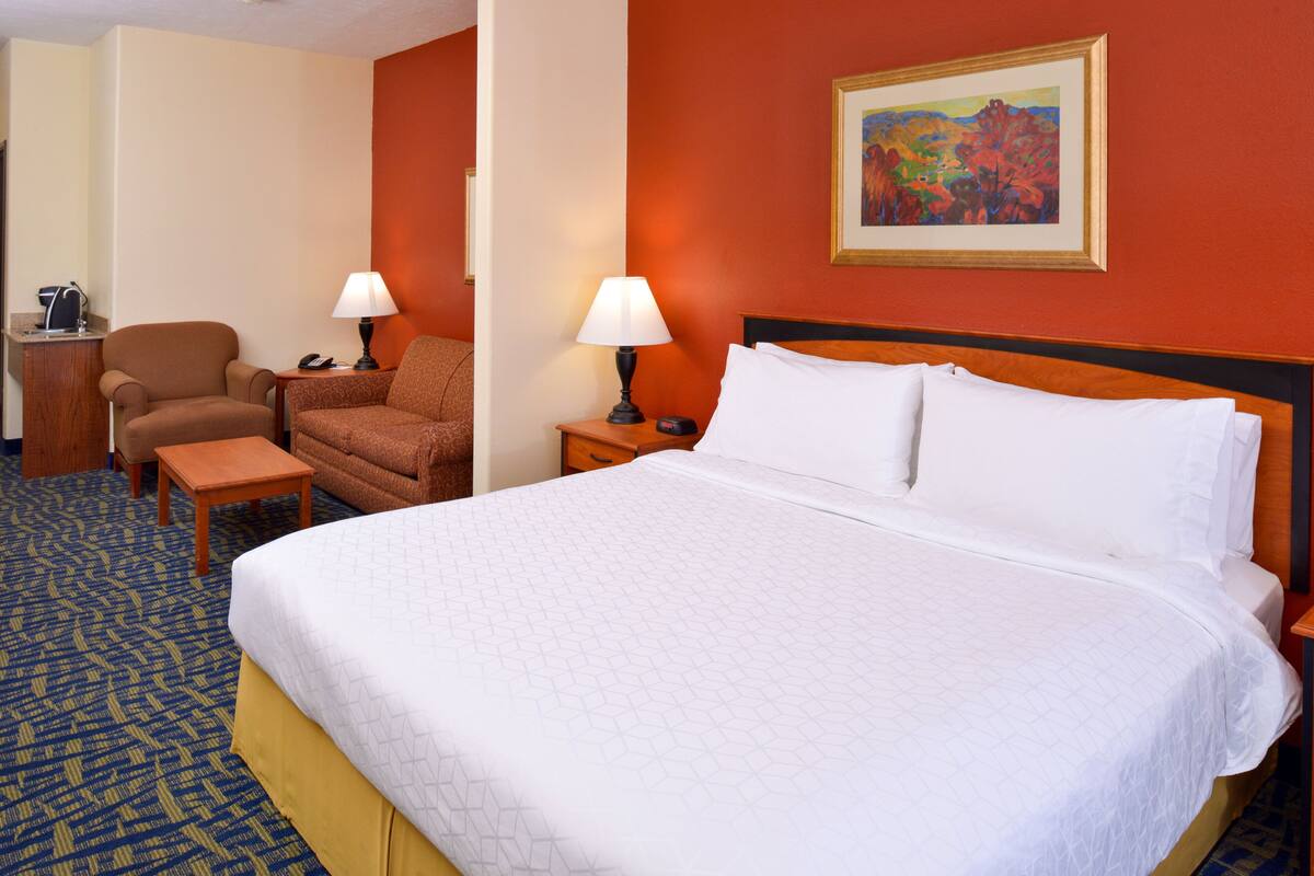 A hotel room with a large bed, two chairs, a desk, and a nightstand with lamps.