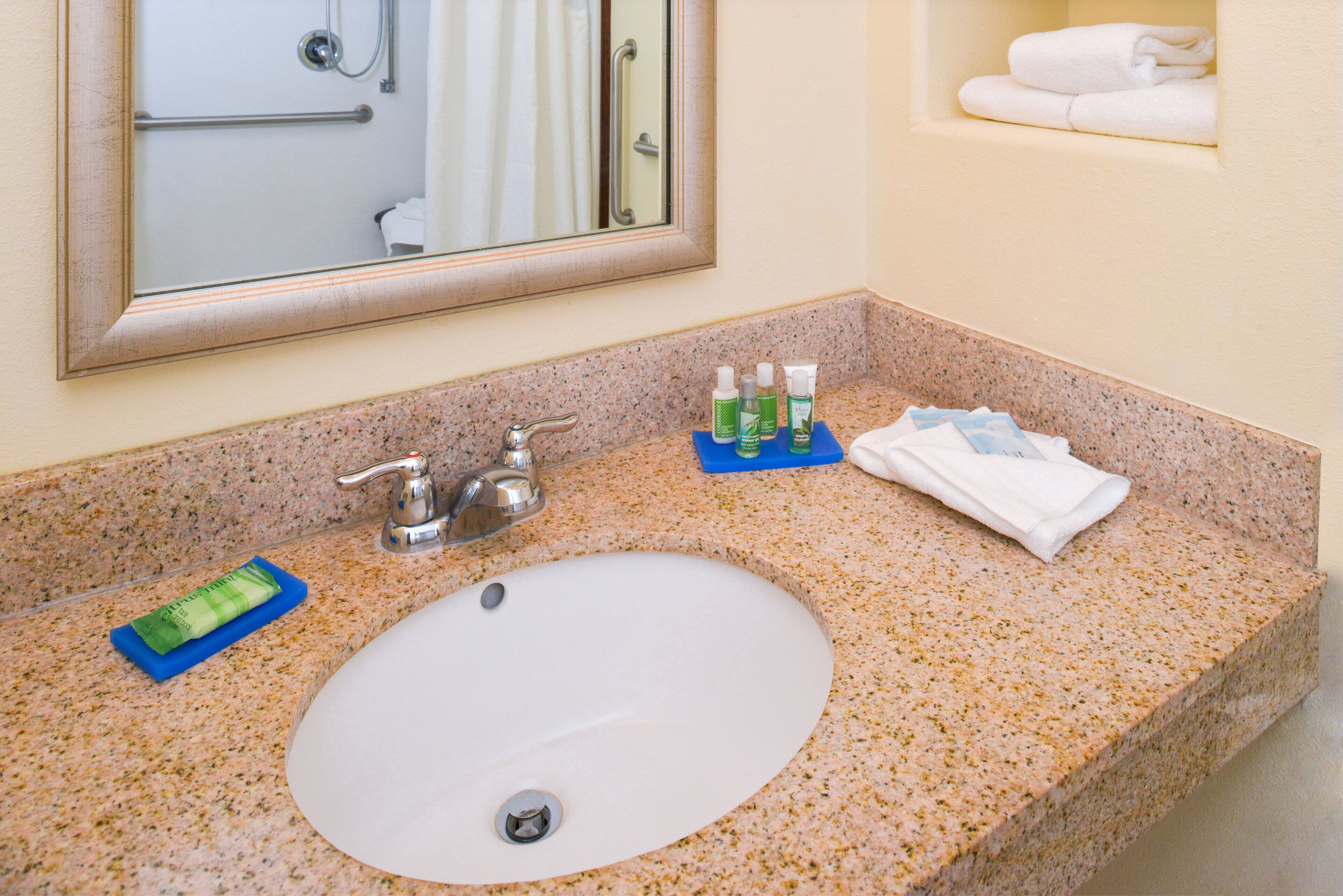 Une salle de bain avec un comptoir en granit, un lavabo blanc, un miroir et un porte-serviettes.