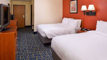 A hotel room with two beds, a desk with a television, and a carpeted floor.