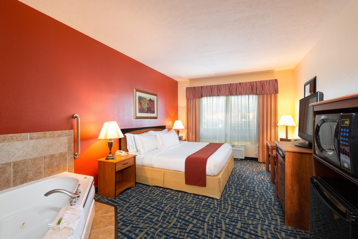 A hotel room with a bed, a TV, a microwave, a desk, a lamp, and a bathroom with a bathtub and sink.