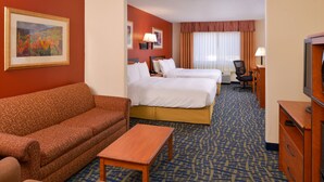 A hotel room with a sofa, two beds, a desk, a TV, and a painting on the wall.