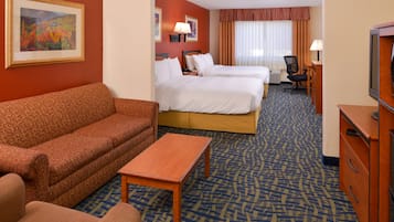 A hotel room with a sofa, two beds, a desk, a TV, and a painting on the wall.