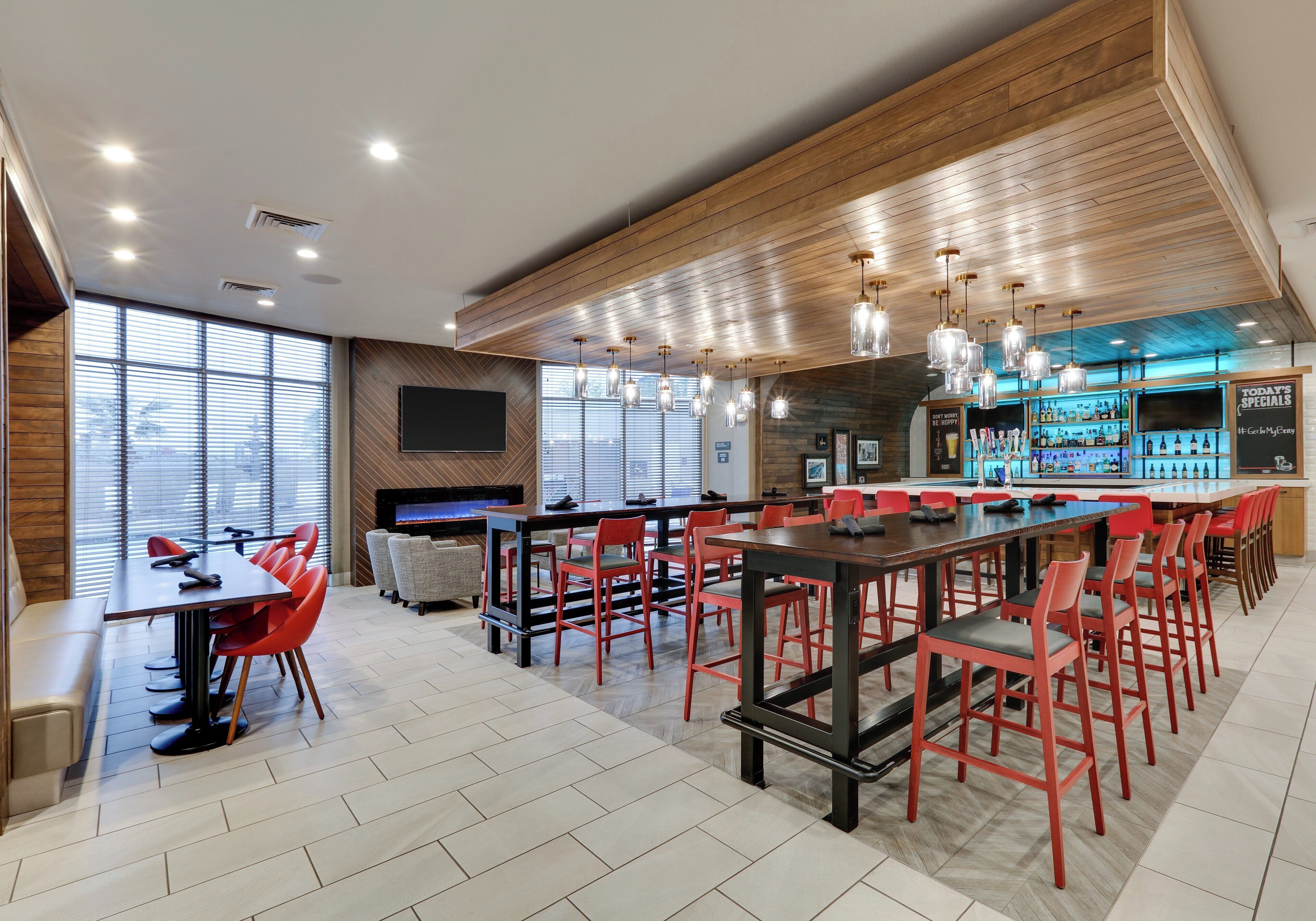 A modern bar area with red chairs, a long table, and a bar counter with a selection of bottles.