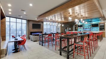 A modern bar area with red chairs, a long table, and a bar counter with a selection of bottles.