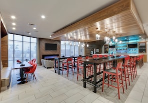 Zona de bar moderna con sillas rojas, una mesa larga y una barra con una selección de botellas.