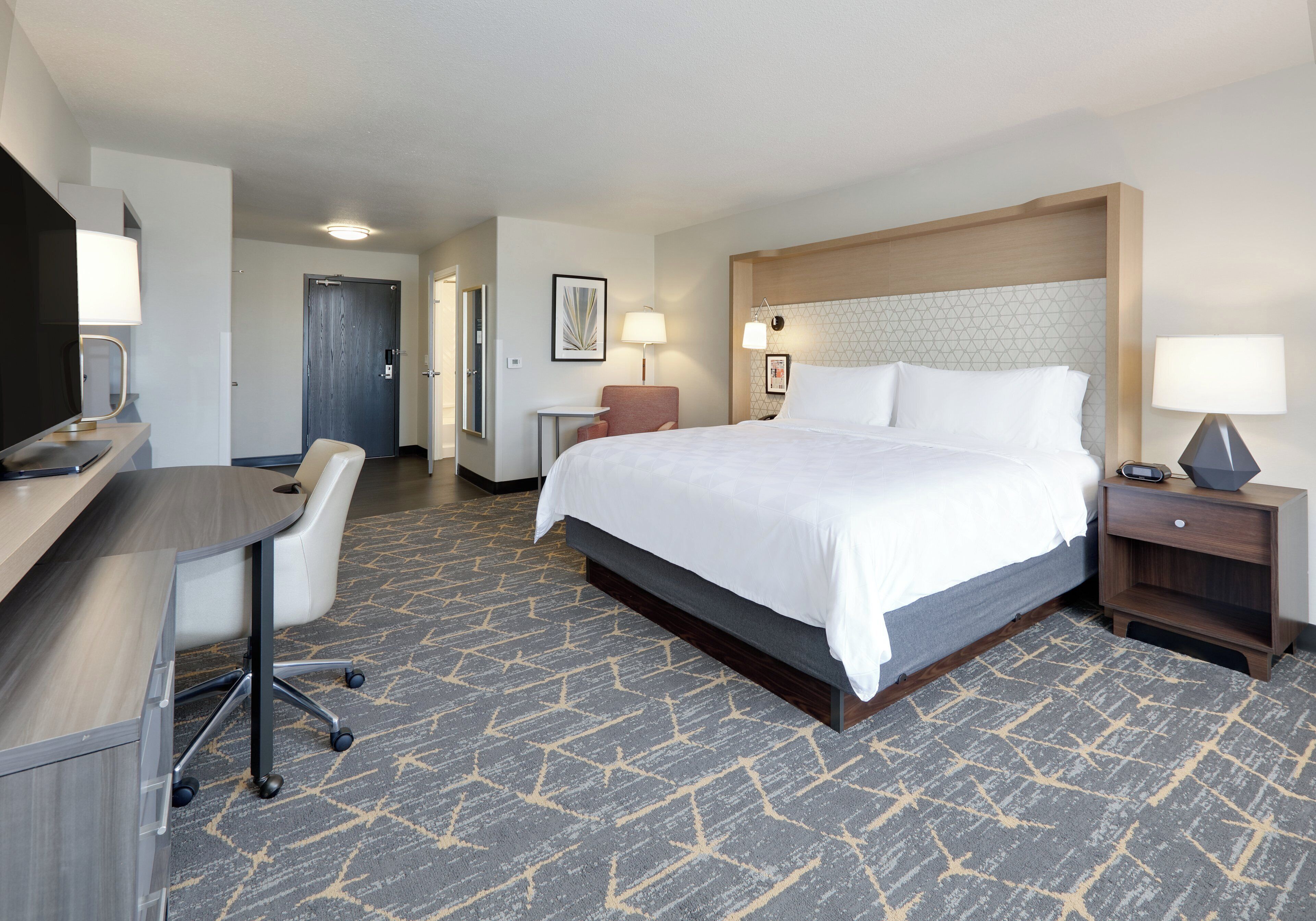 A hotel room with a bed, desk, chair, and a small table.