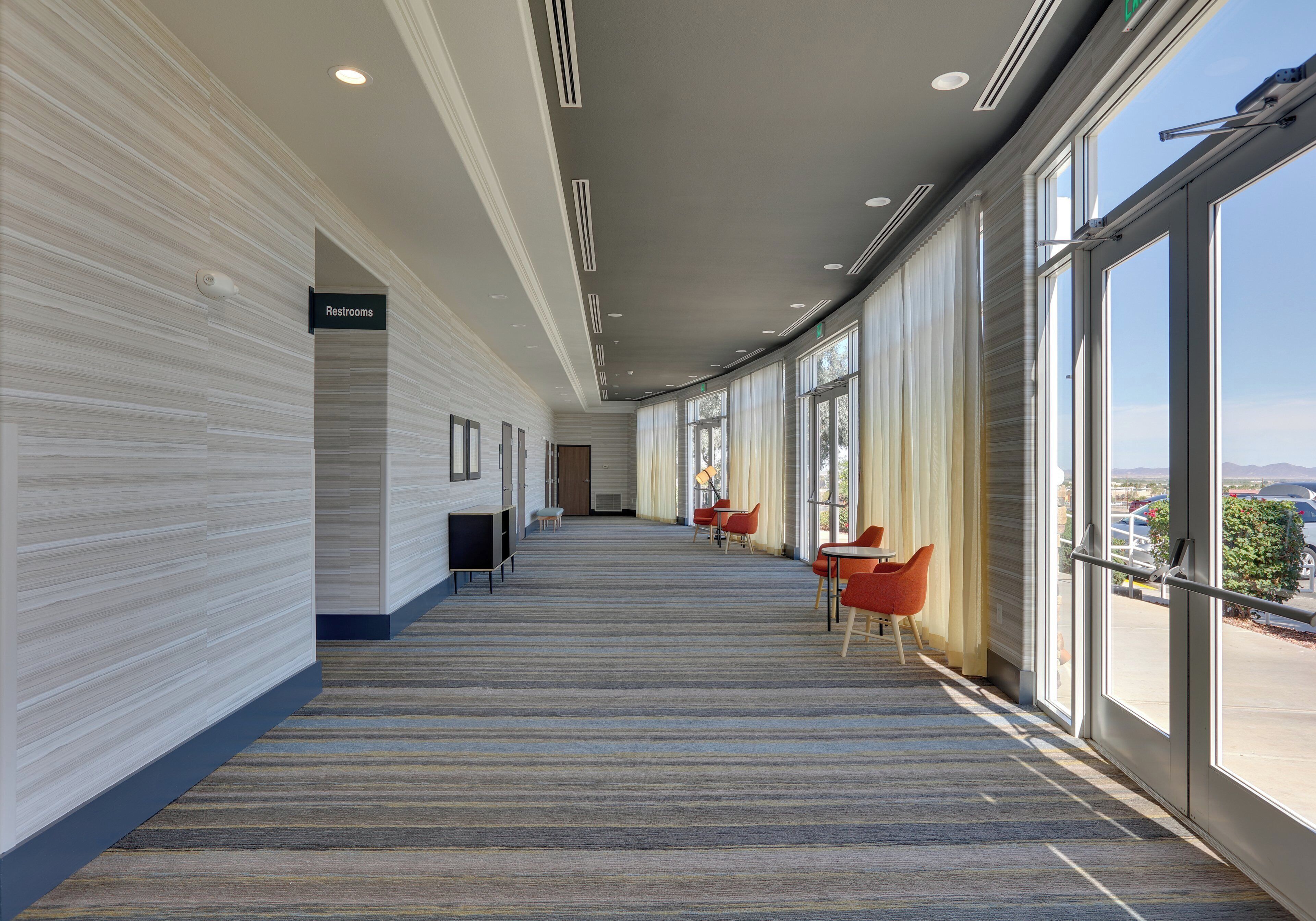 A corridor with a sign for restrooms, a door, and seating areas with tables and chairs.