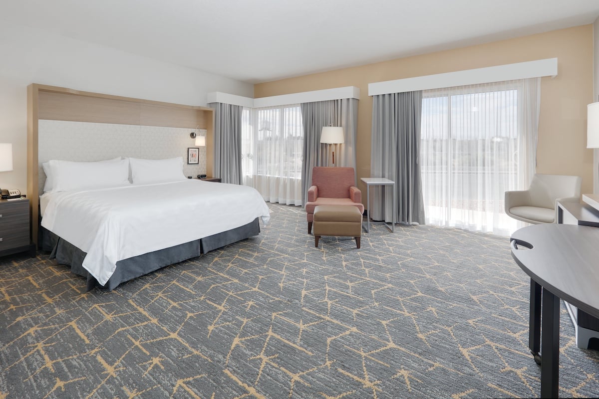 A hotel room with a large bed, a desk, a chair, and a small table.