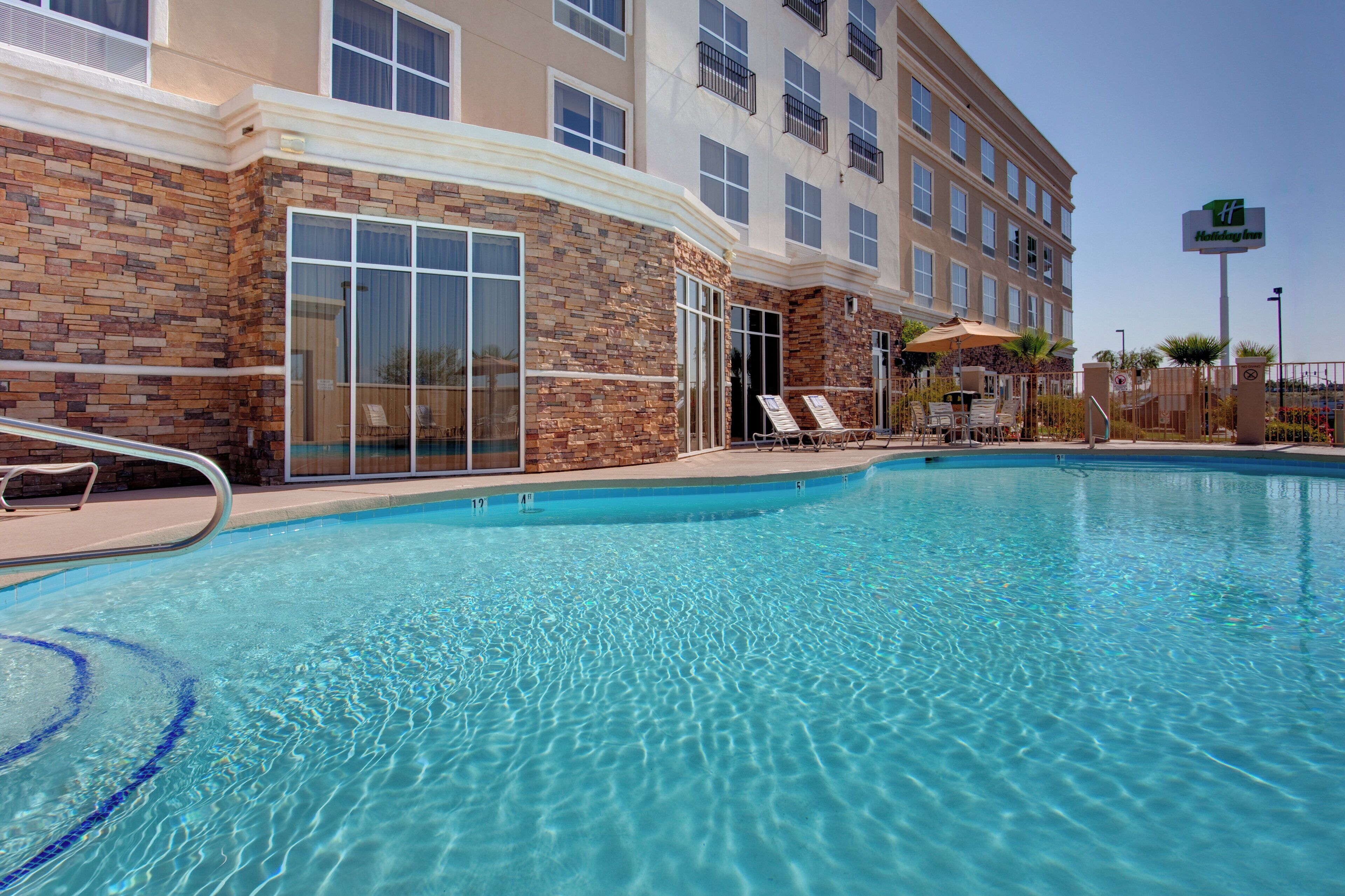 A hotel with a swimming pool, outdoor seating, and a brick facade.