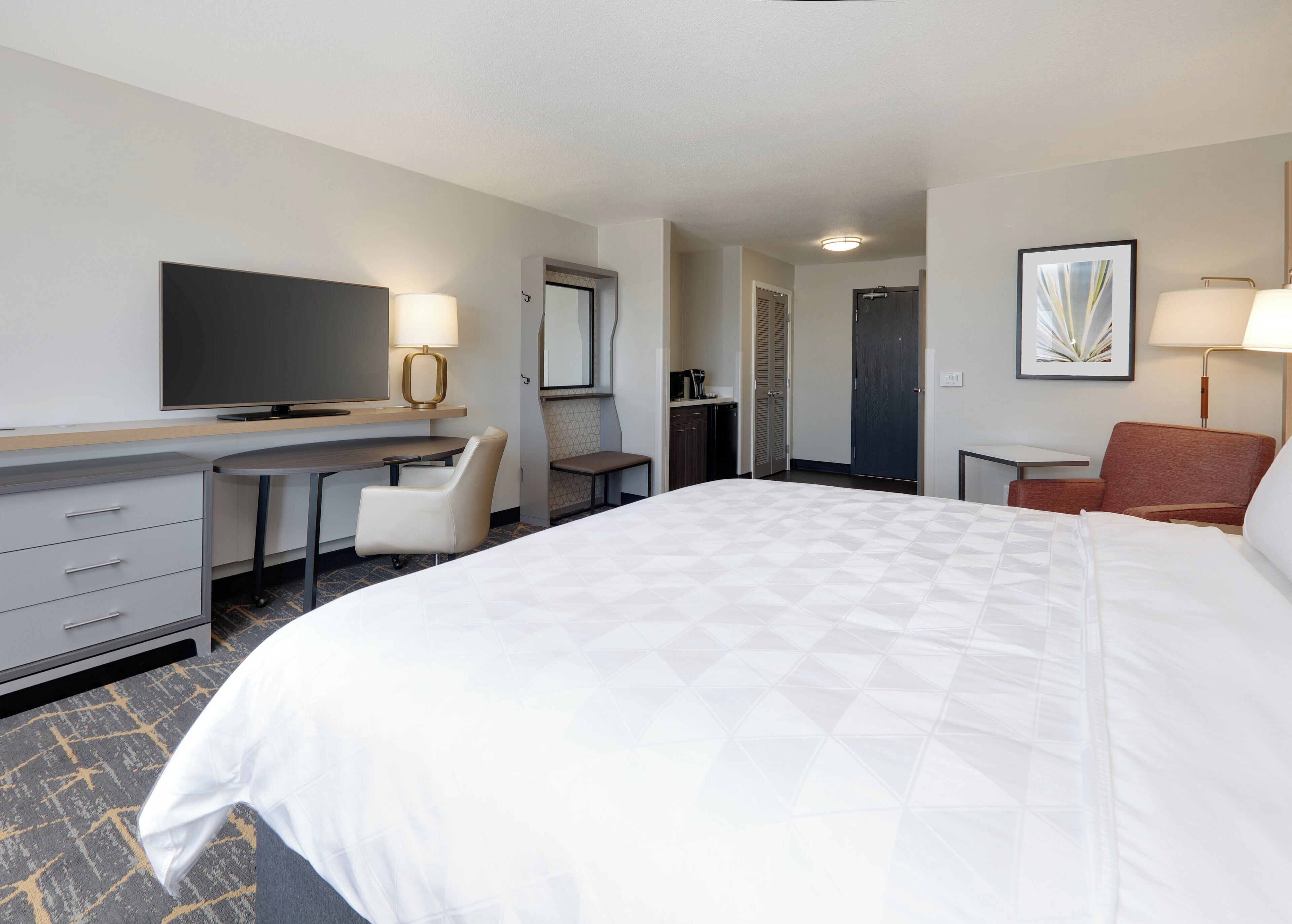 A hotel room with a bed, desk, chair, television, and a door leading to a bathroom.