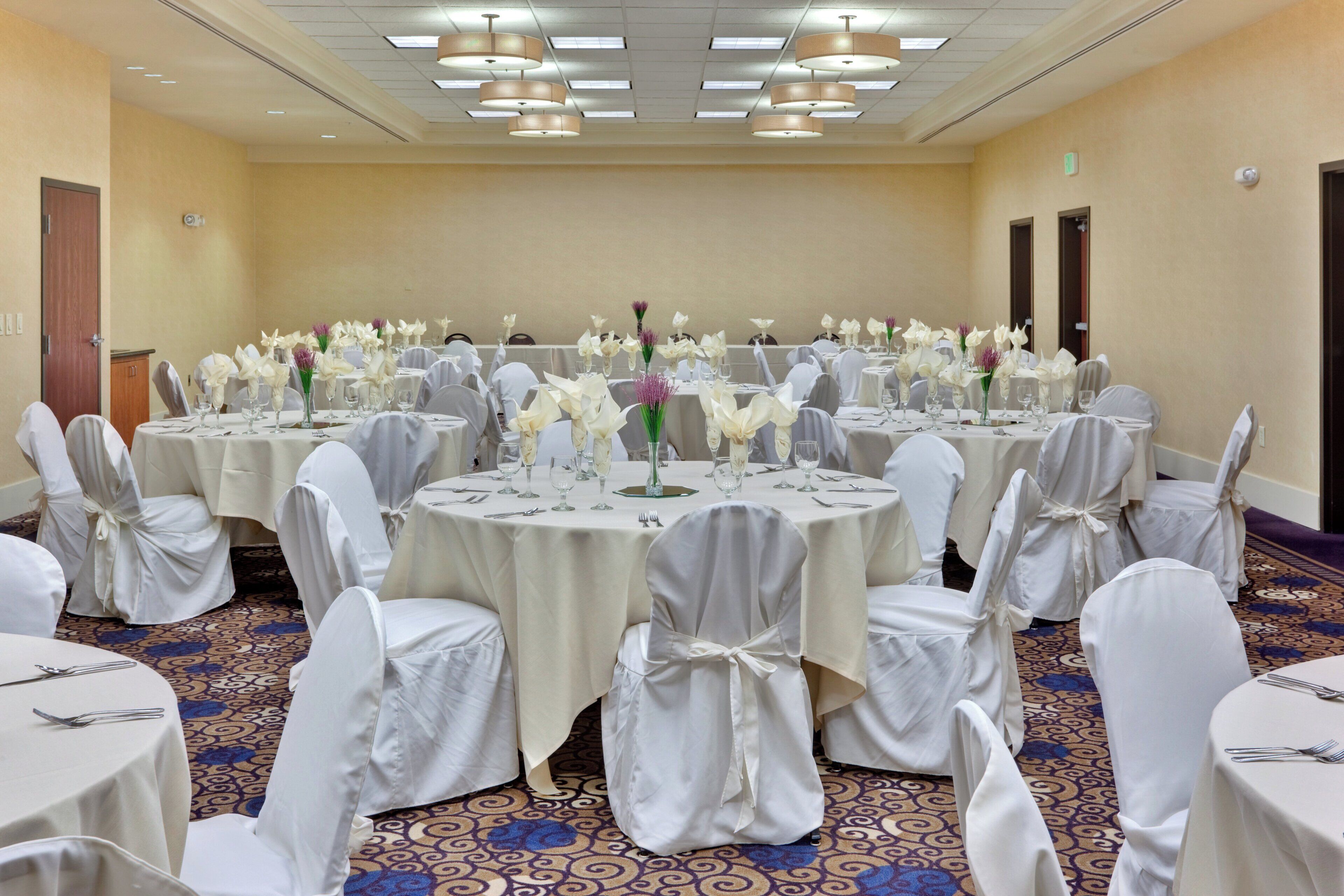 Un salón de banquetes con mesas redondas dispuestas para un evento formal, con manteles blancos y centros de mesa florales.
