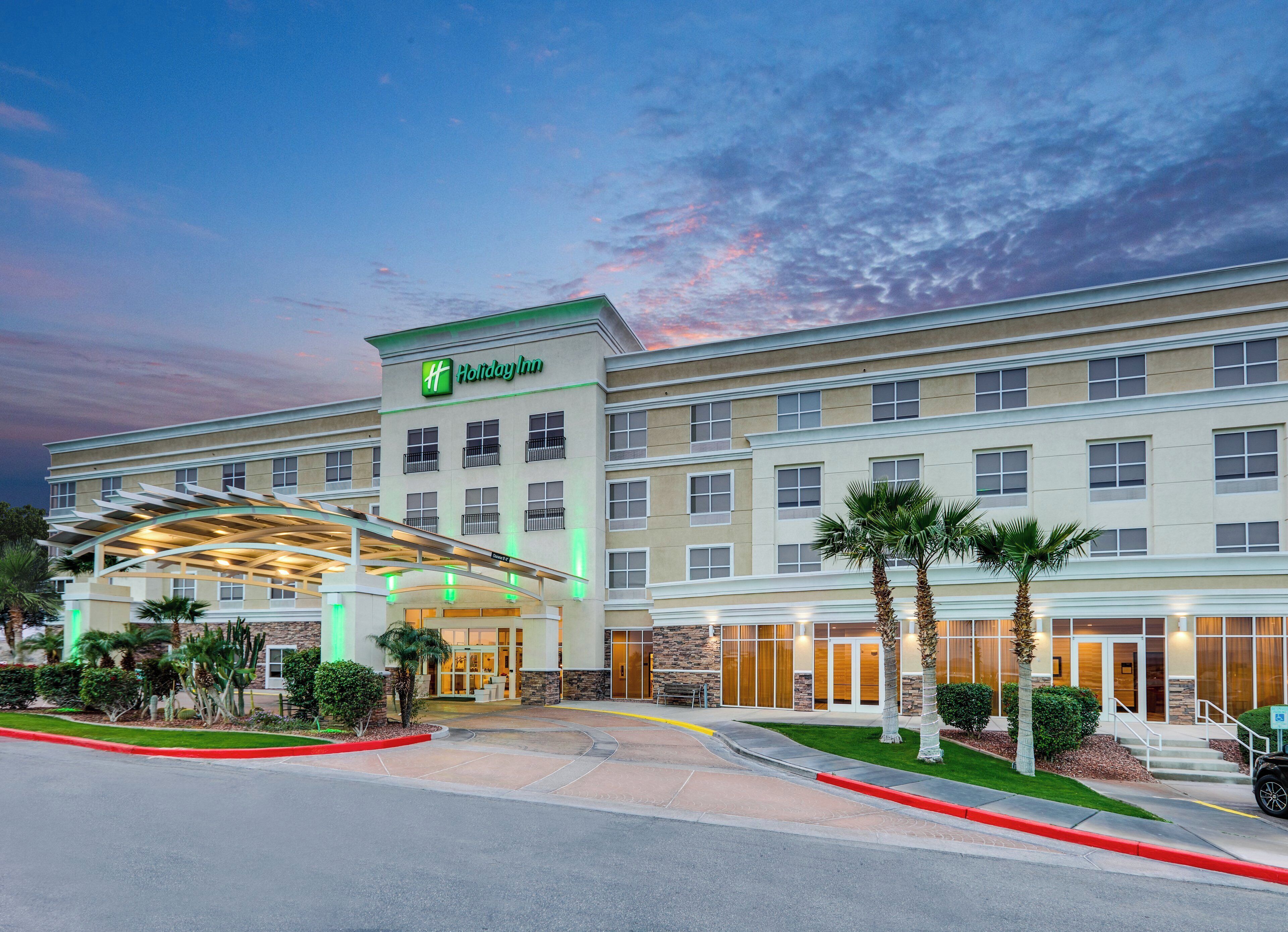 Un hotel Holiday Inn con entrada cubierta, varios pisos y un jardín delantero ajardinado.