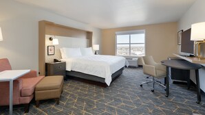 Une chambre d’hôtel équipée d’un lit, d’un bureau, d’une chaise et d’une grande fenêtre donnant sur la ville.