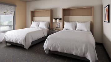 A hotel room with two beds, a window with a view, and a wall-mounted lamp.